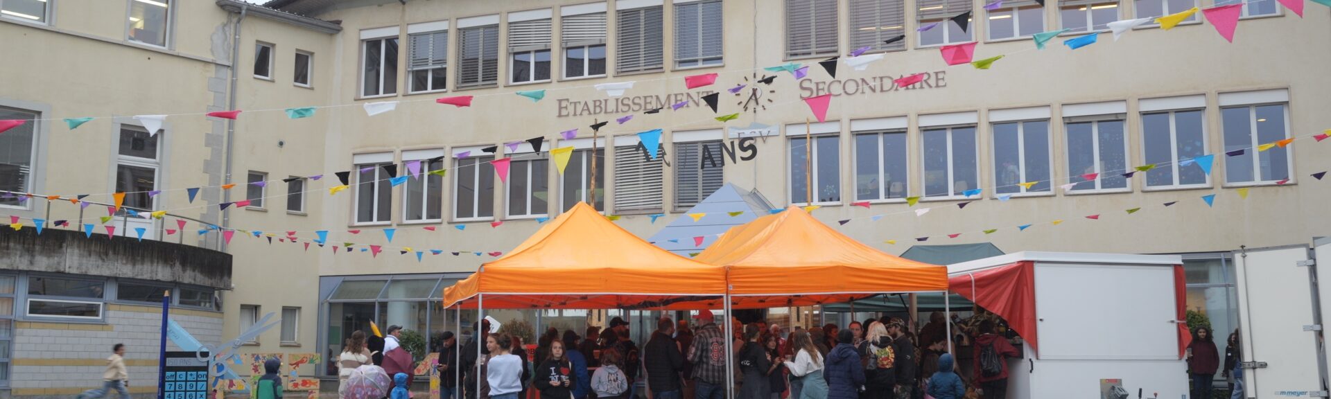 Façade de l’établissement secondaire de la Vallée de Joux, décorée de fanions, avec des visiteurs sous des tentes orange.